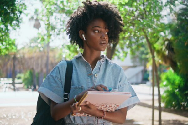 African teenager walking street sunny day holding books closeup. Woman strolling